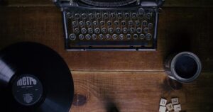 A typewriter and a vynal record rest on a wood desk.