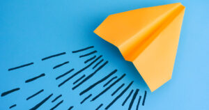 A yellow paper airplane sits on a blue desk with draw air current behind it.