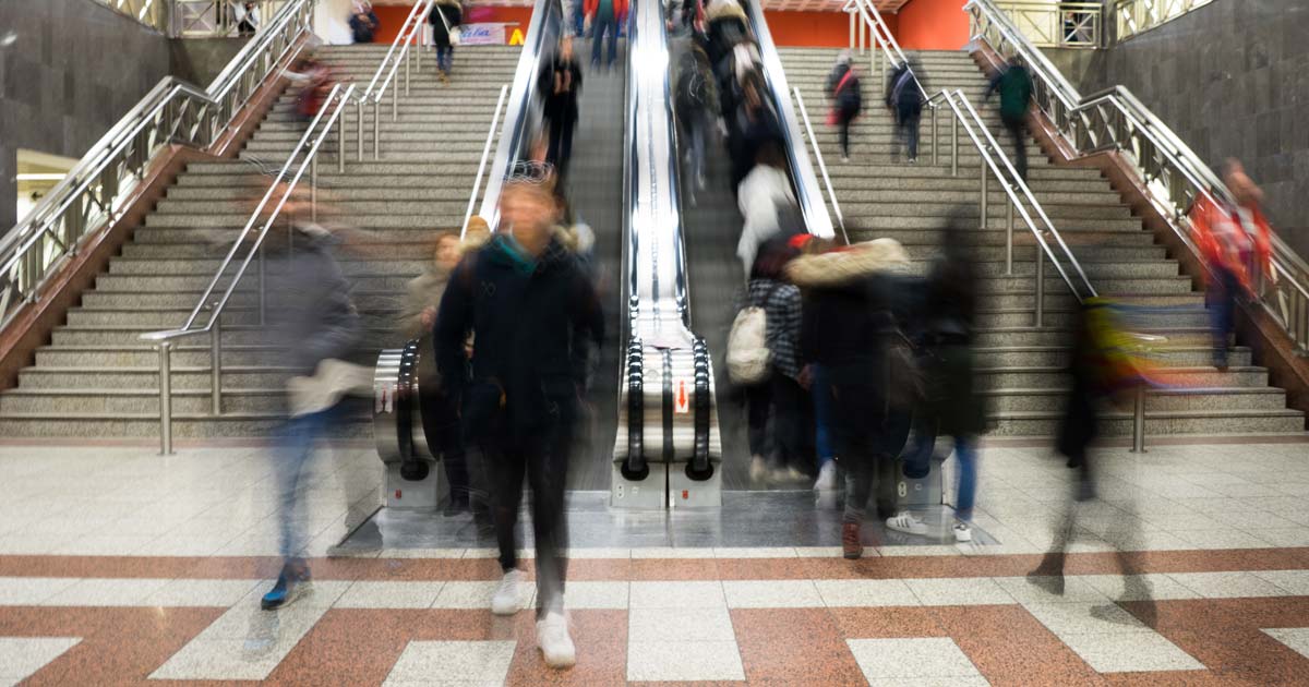 Transit riders are a blur in a subway station with stairs and an escalator.