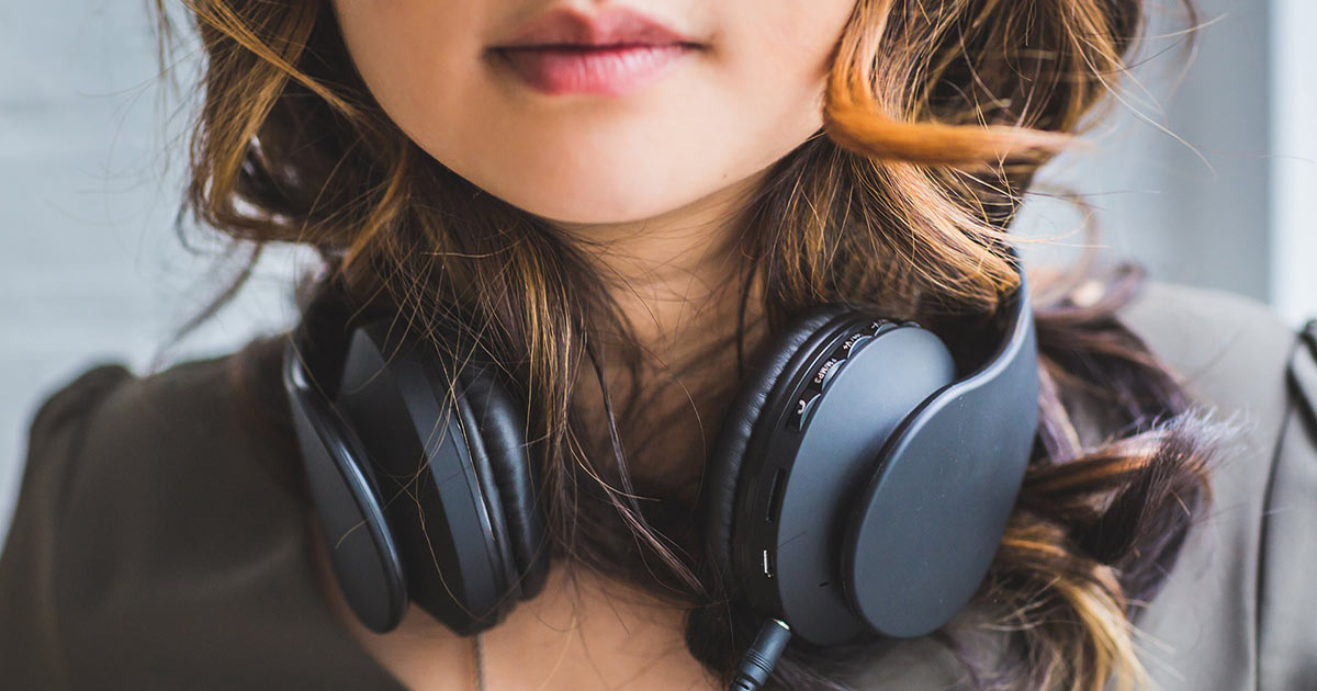 A close up of a woman resting her headphones on her neck around her shoulders.