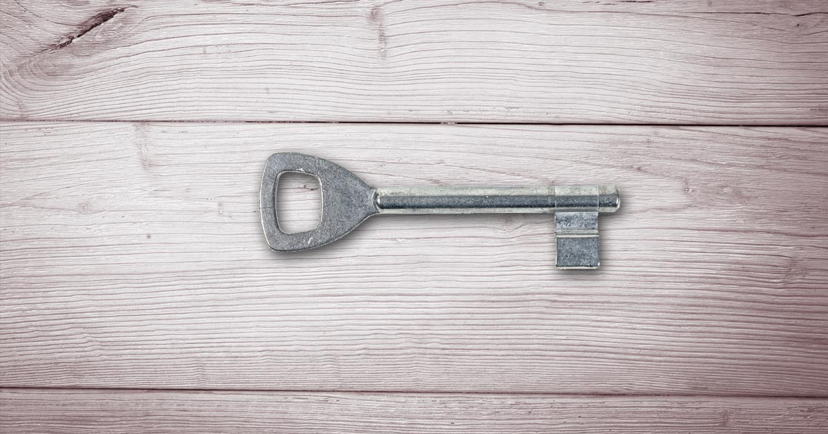 A simplistic vintage key rests on a wood table.