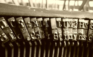 An assortment of metal letters for a printing press lined up against an out of focus metal background.