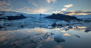 Ice covered mountains loom in the background, with ice and snow floating in the cold waters of the artic.