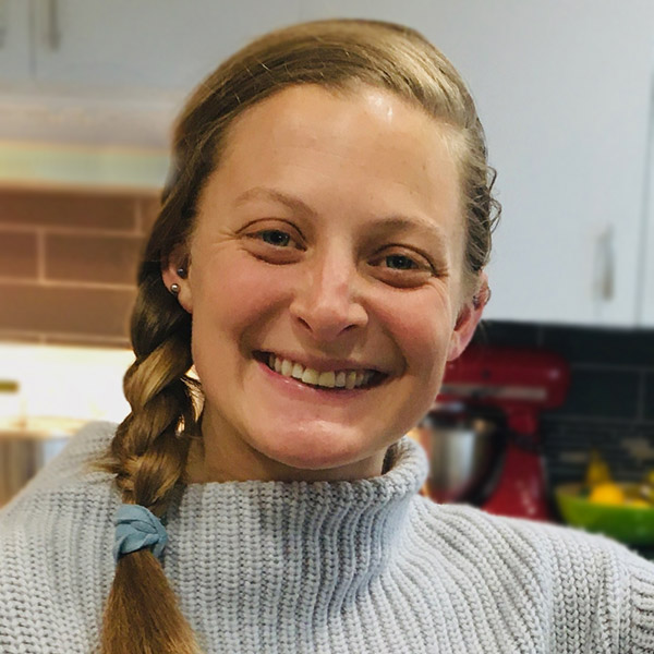 Ryan Cope profile photo in her kitchen with a light blue sweater and her red hair.
