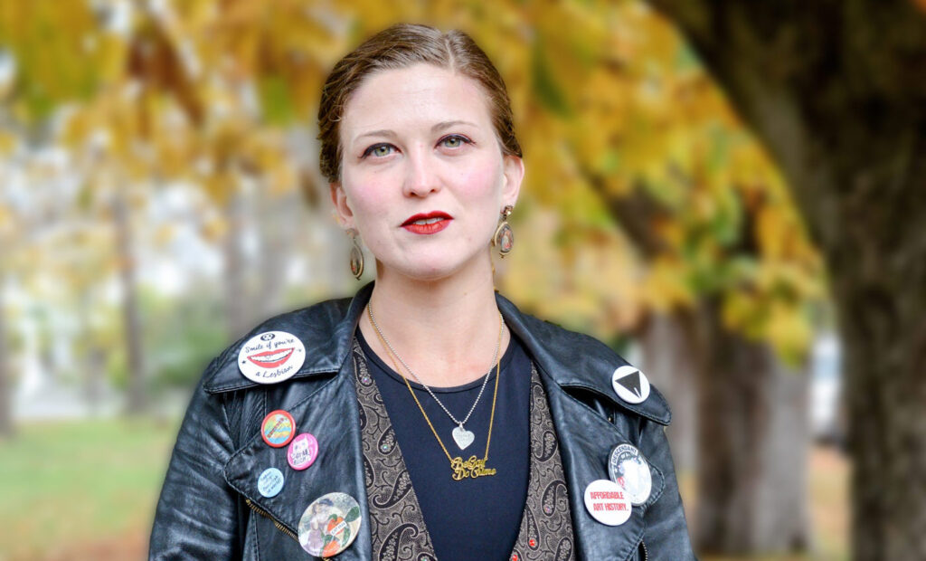 Baylee Woodley, PhD, stands amongst the trees and autumn leaves near Dallas Road, Victoria, BC.